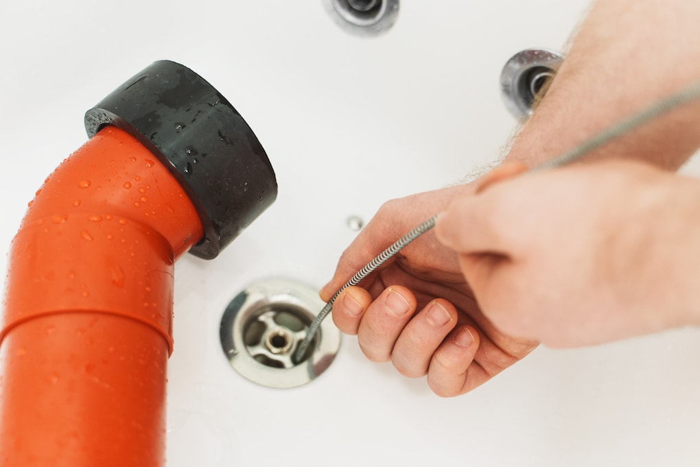 Plumber using drain snake to unclog bathtub.