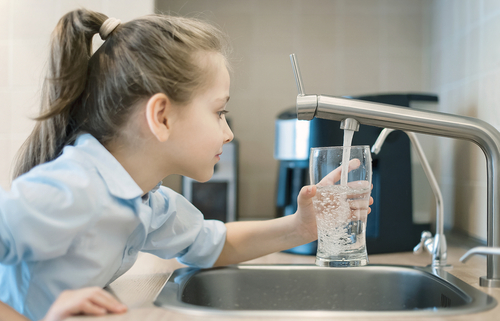 A young girl fills up a glass of water from the tap in her kitchen.