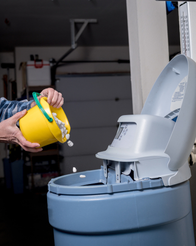 A homeowner pours salt pellets into their water softener.