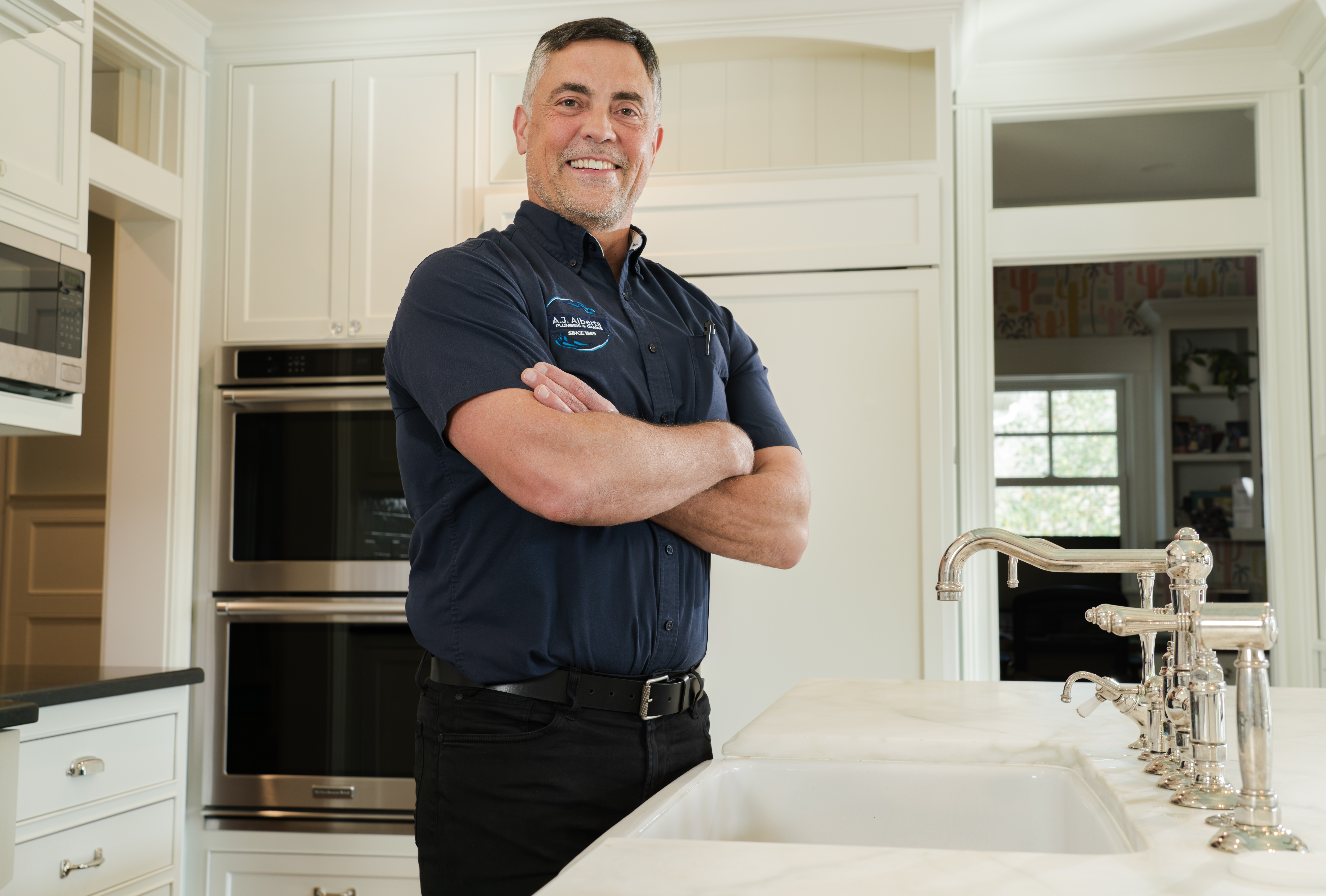 Steve Grohn of A.J. Alberts Plumbing stands in a kitchen with his arms crossed.