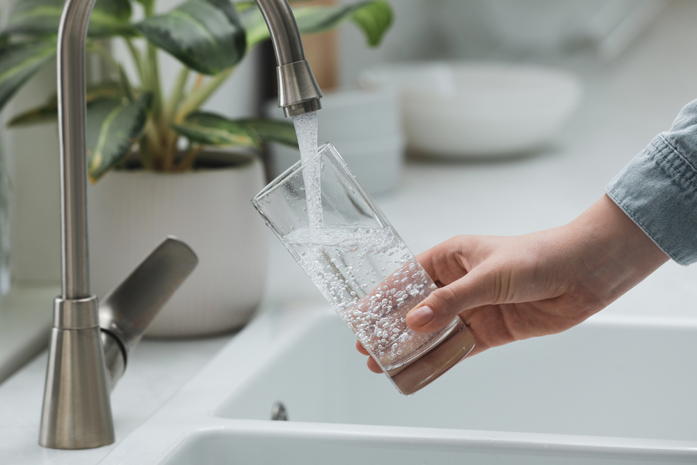 A person fills up a water glass from their kitchen tap.