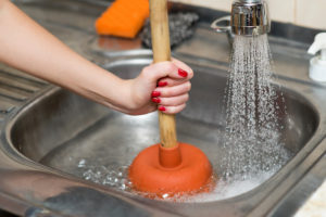 woman cleans plunger with clogged sink, close up